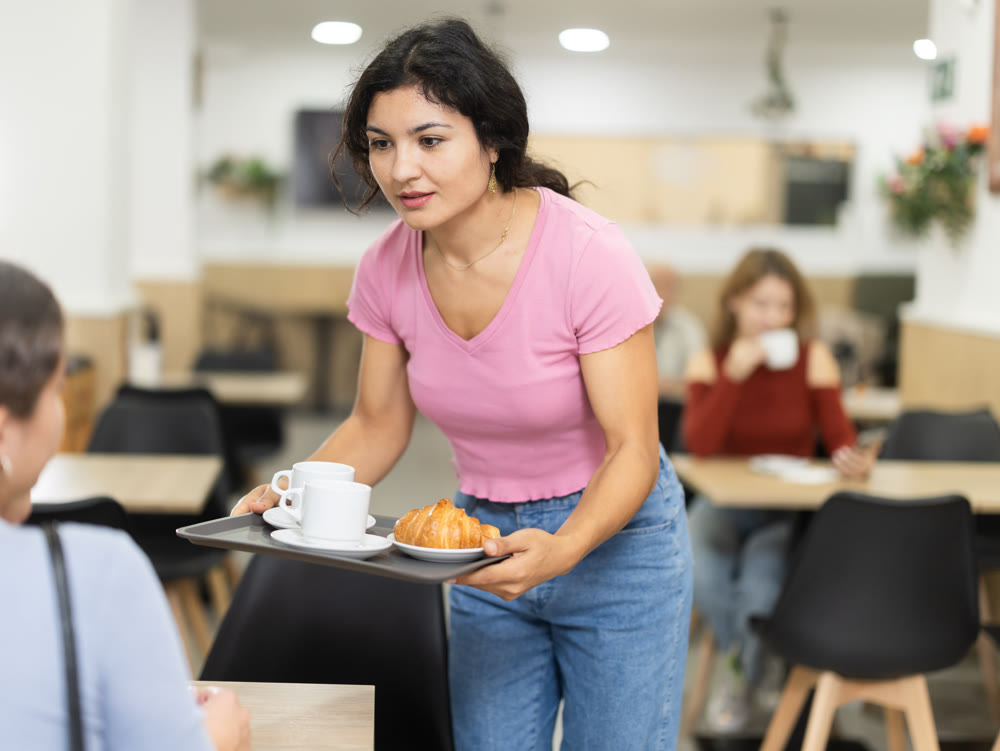 Woman with two cups of coffee on tray goes to table in cafe, having coffee break with friends, colleagues