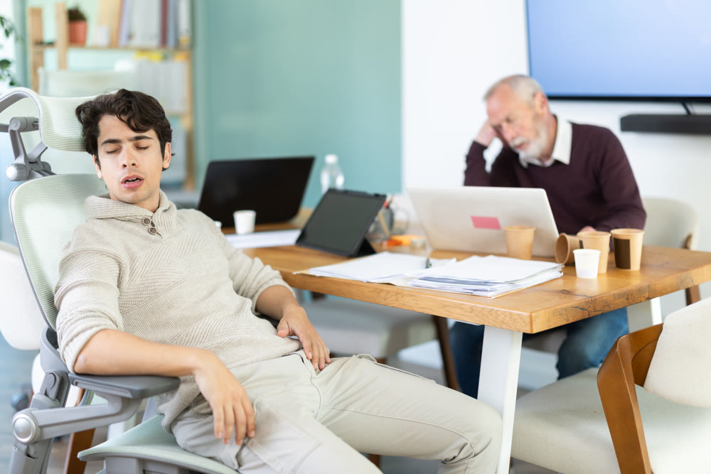 Wearied senior man and guy colleagues are dozing near workplace in office