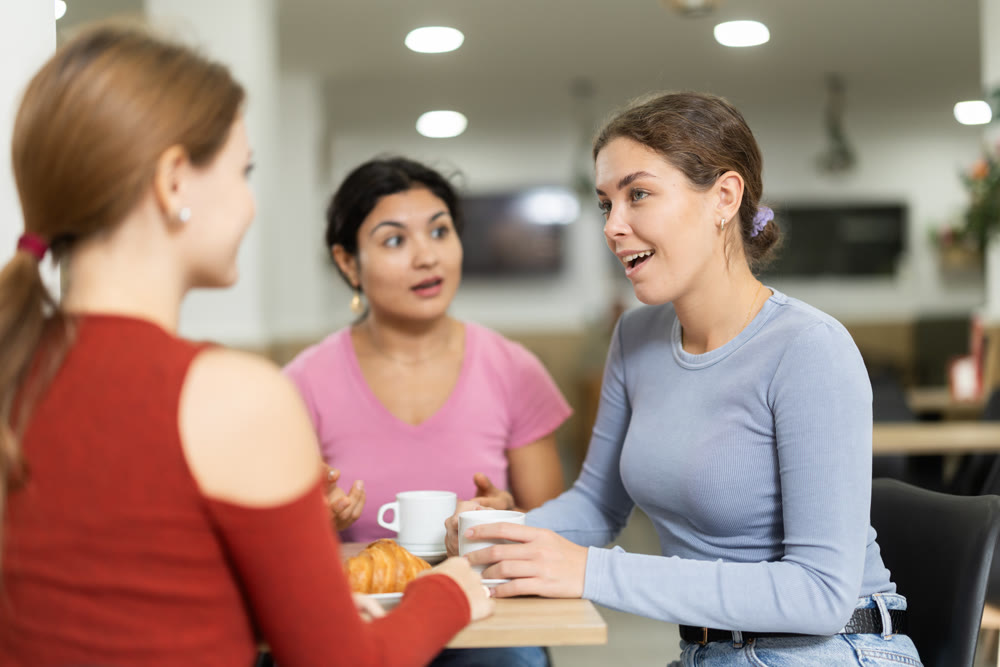Three girlfriend chatting over coffee and croissant in cafeteria