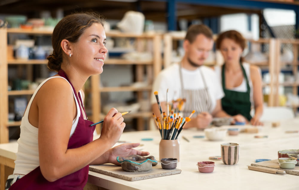 Girl in apron designing handmade clay plate with brush in taller room