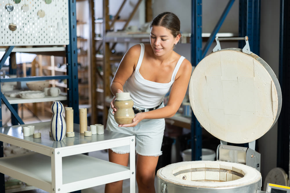 European girl in apron takes ready-made pottery made of clay out of oven