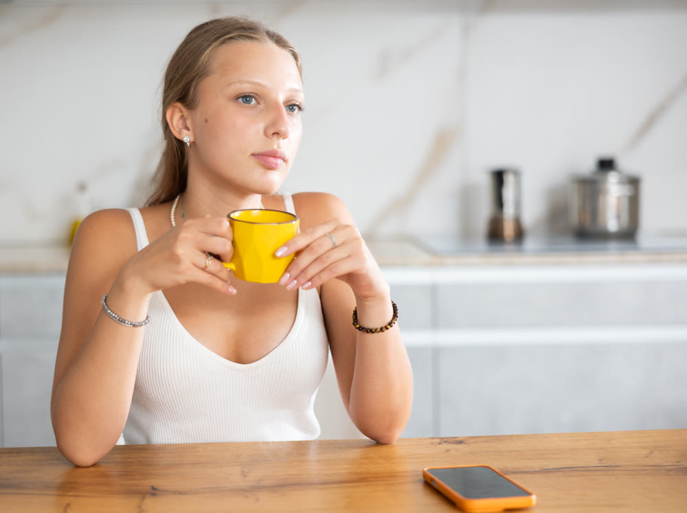 Young woman in shorts drinking coffee in kitchen