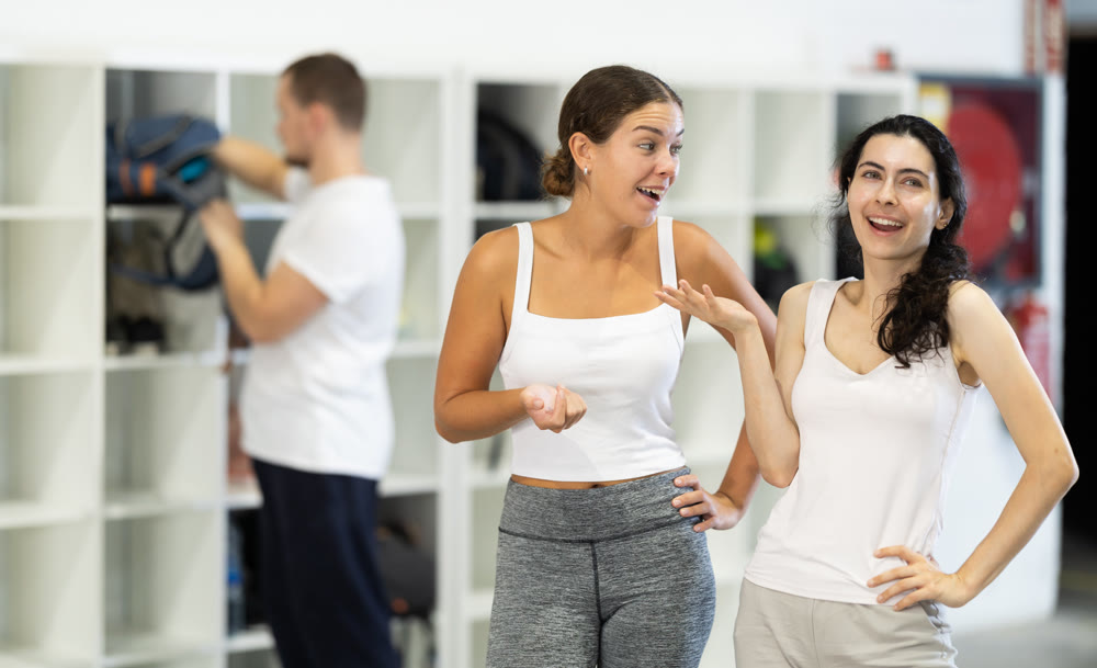 Two female climbers laughing and sharing stories in climbing gym locker room after exciting successful workout