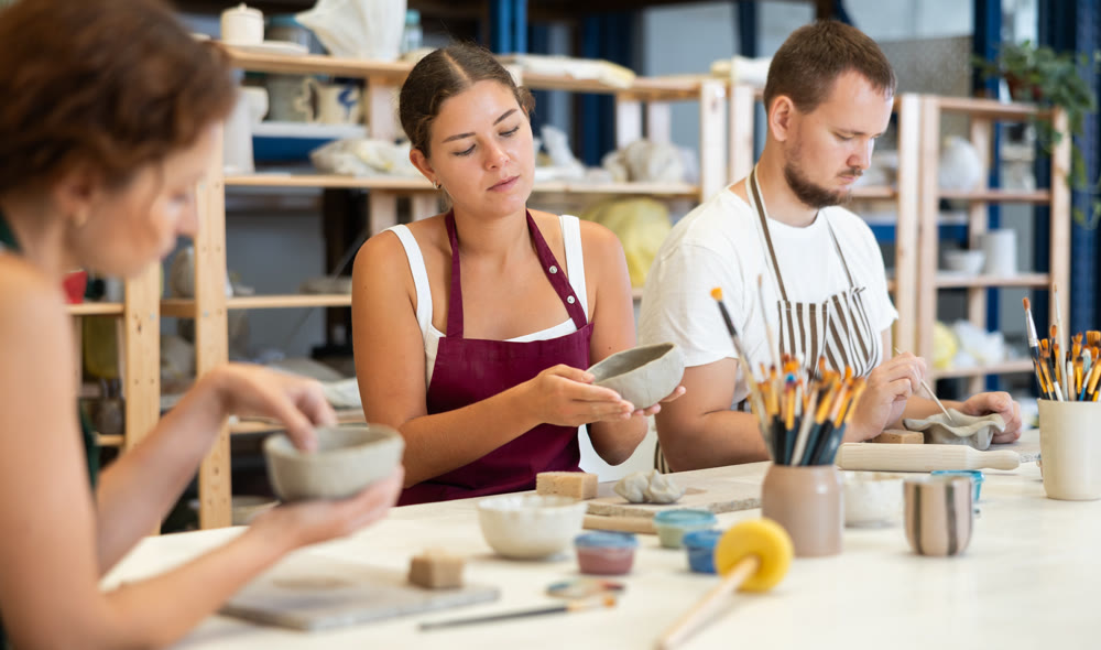 Three pottery workshop workers sculpt from raw clay