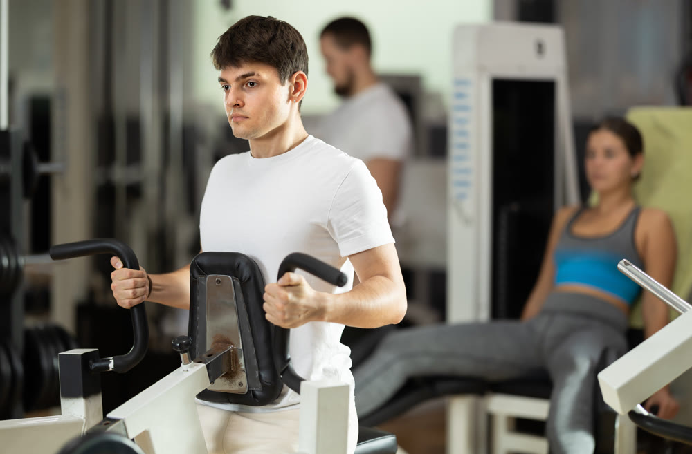 Guy in gym performs exercises for arm muscles using simulators and fitness center equipment.
