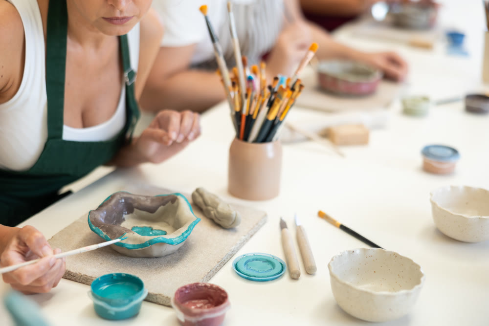 Close up girl paints bowl of clay during master class, top view.