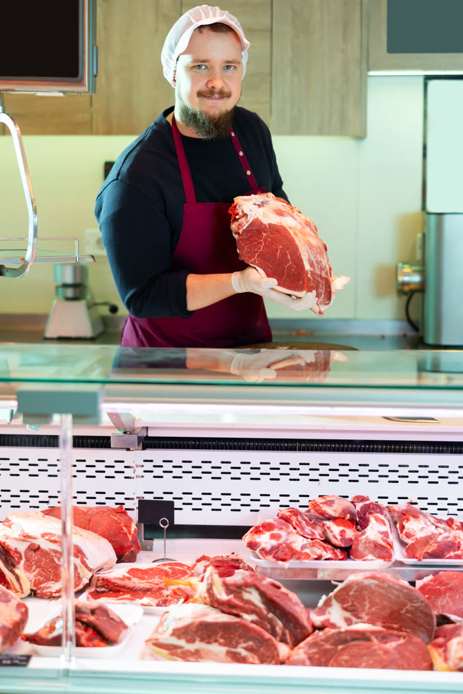 Male butcher putting raw meat on supermarket display