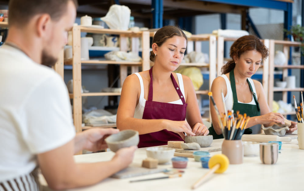 Three pottery workshop workers sculpt from raw clay