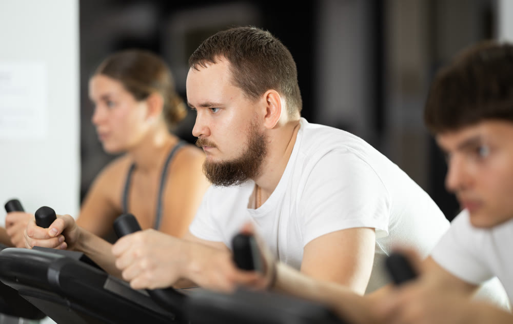 Focused bearded man works out with stationary bicycle during class at fitness club