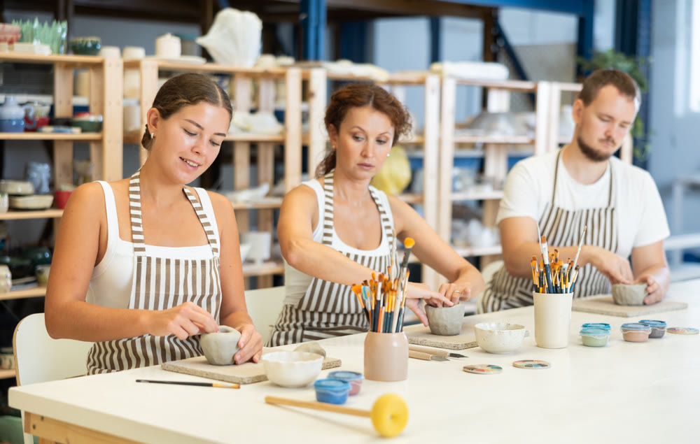 Three pottery students mold clay into homemade plates and other utensils