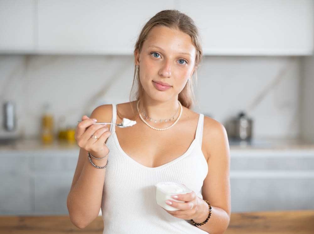 Young woman eating yogurt in kitchen