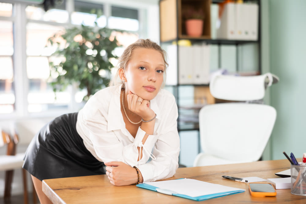 Young woman standing leaning on desk in office