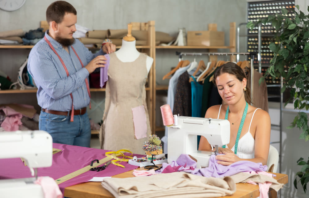 Male dressmaker working with mannequin while girl sews