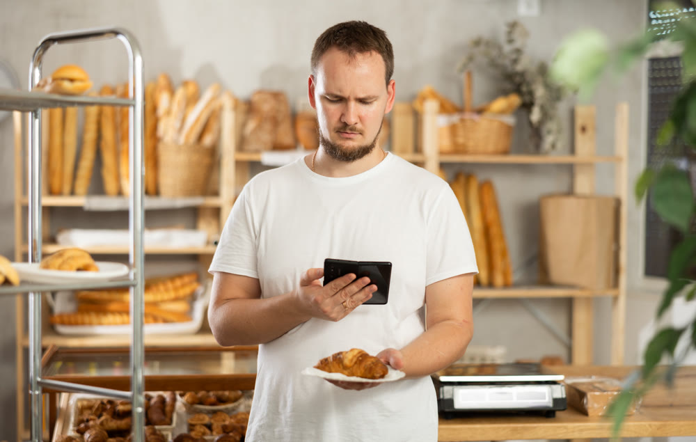 European male customer with phone takes pictures of croissant in disposable plate dish