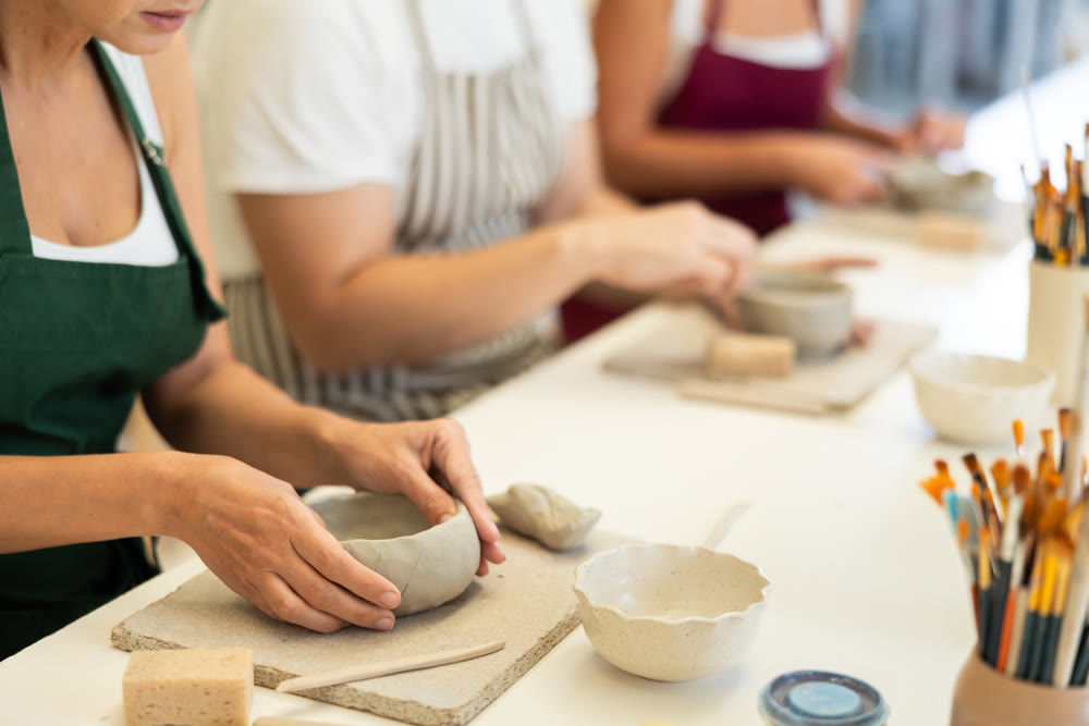 Closeup of female hands molding clay into plate in pottery workshop