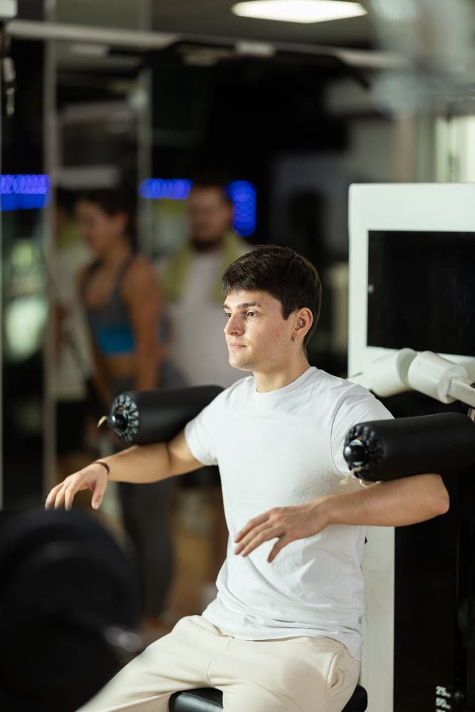 Guy in gym performs exercises for arm muscles using simulators and fitness center equipment.