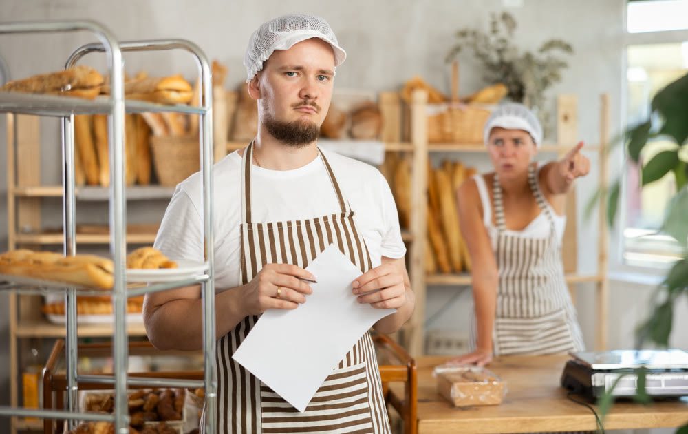 In bakery, frustrated male employee with paper during quarrel with girl boss
