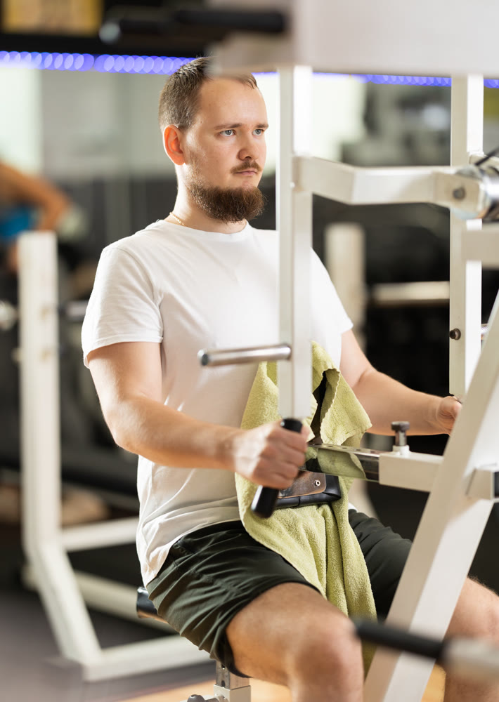 Bearded man in gym performs exercises for arm muscles using simulators and fitness center equipment.