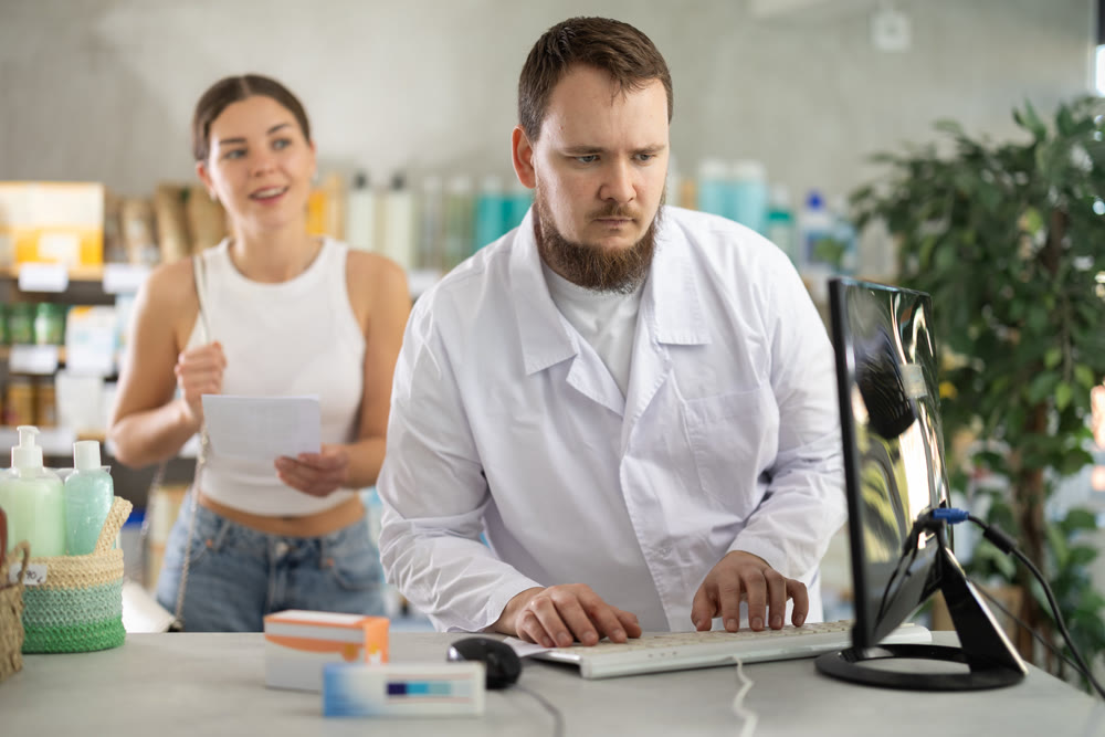 Male pharmacist helps female customer find prescription medication
