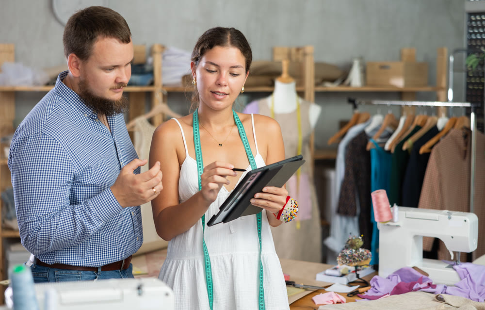 Young female dressmaker discussing with man the sketch on tablet