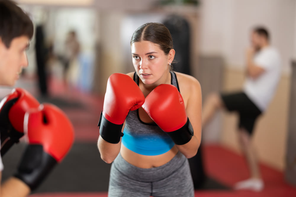 Girl punches, tries to defeat guy opponent during training fight in ring.