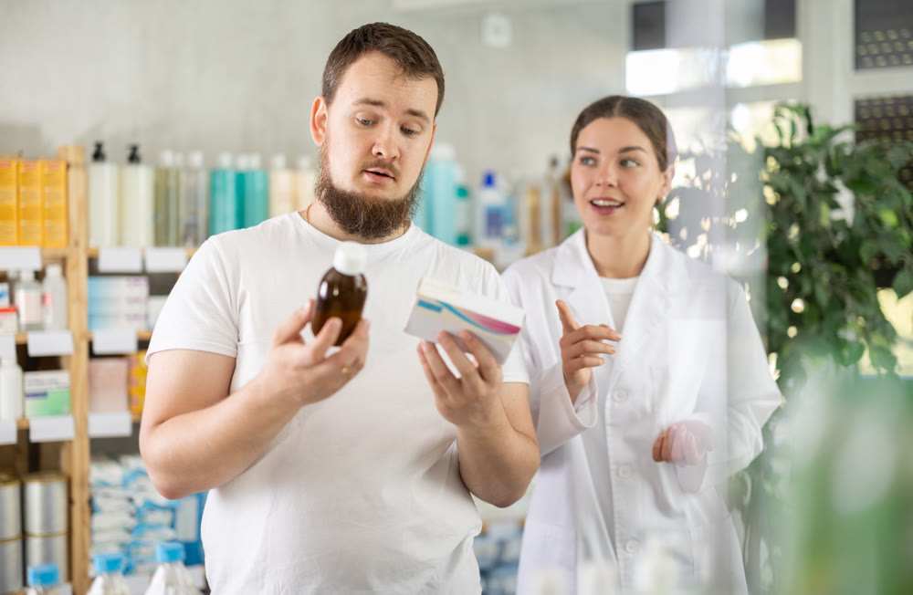 Man chooses cough syrup in modern pharmacy. Female pharmacist helps with choosing medicine