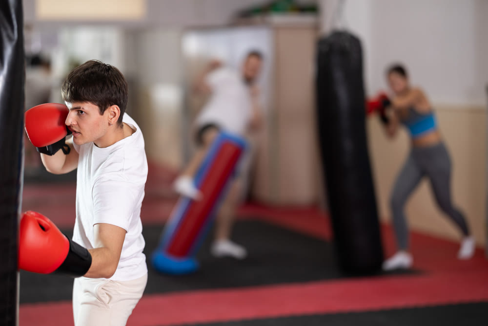 Guy punches and kicks punching bag in gym.