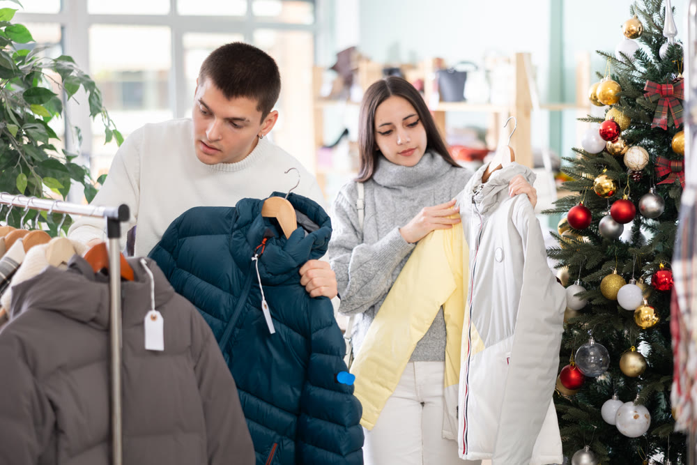 Portrait of happy married couple choose coat or jacket for girl against background of Christmas tree in store