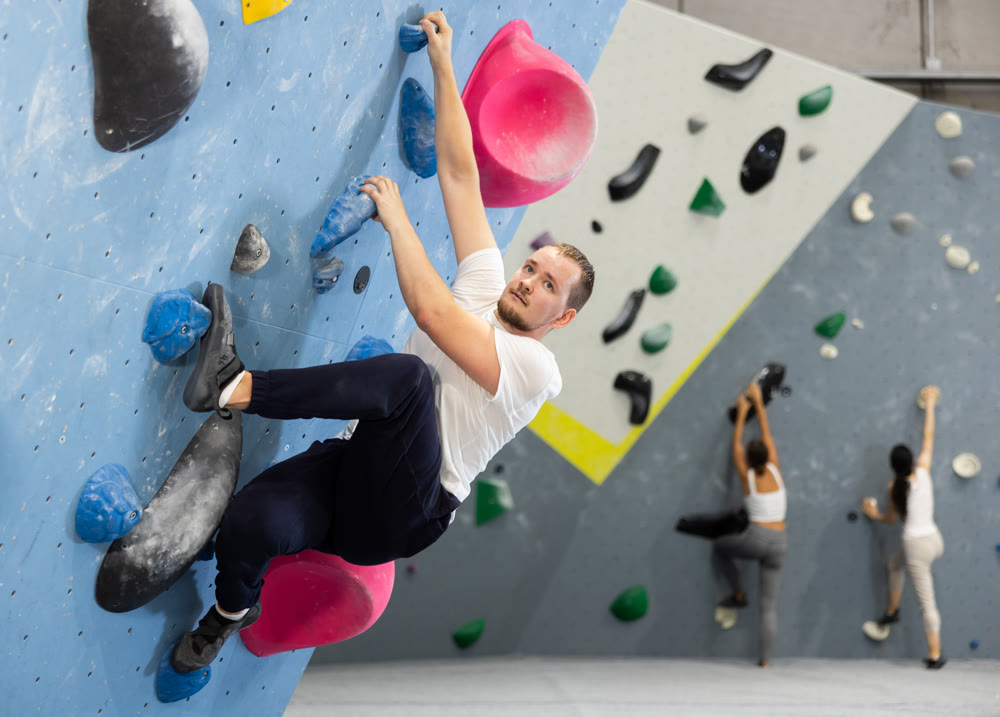 Man climbing a tall, indoor, man made rock climbing wall
