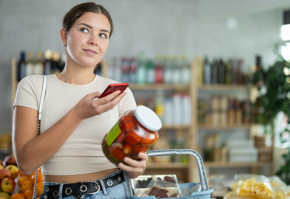 European woman customer at shop scans QR code on pickled tomatoes jar using phone camera