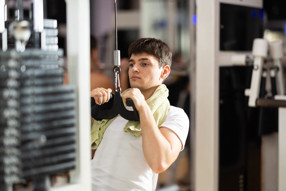 Guy in gym performs exercises for arm muscles using cable crossover machine and pull weighted rope