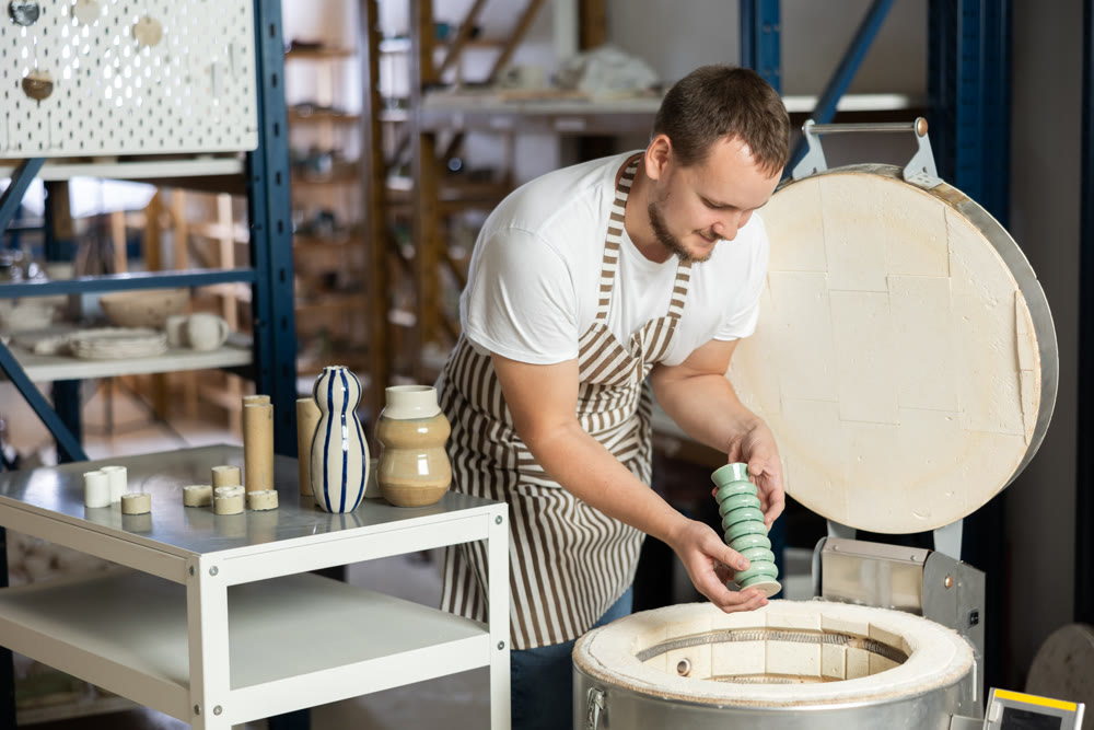 European guy in apron takes ready-made pottery made of clay out of oven