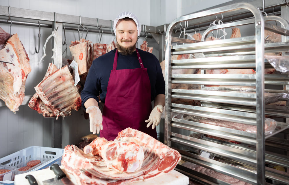 Bearded butcher shop seller preparing beef cuts for sale