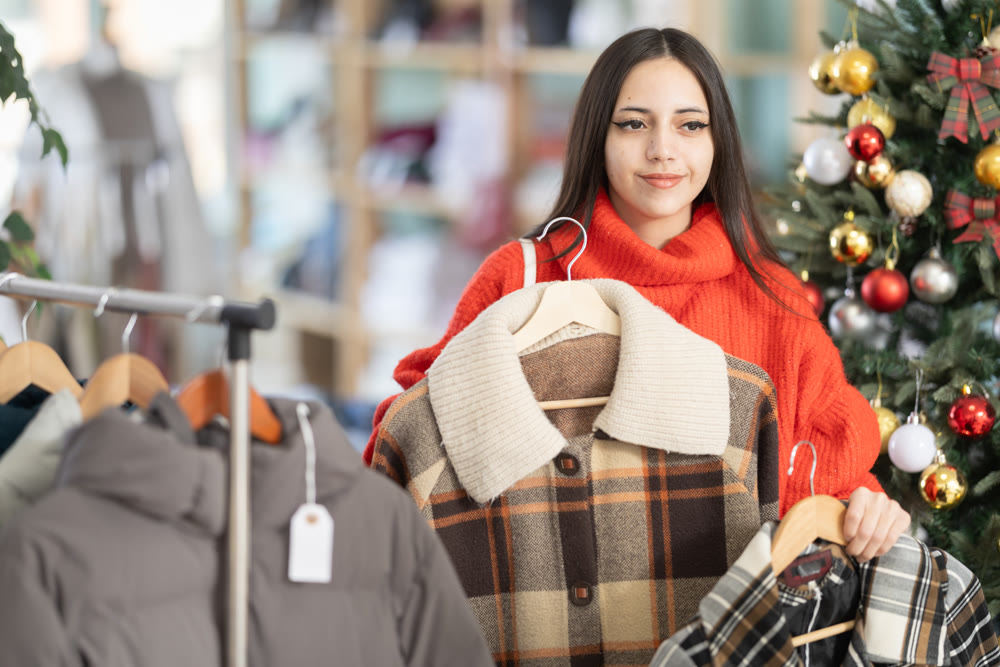 Young woman chooses coat or down jacket in clothing store
