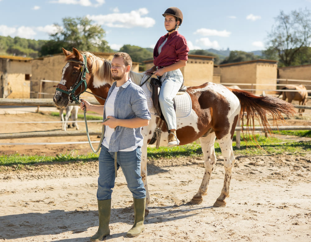 Young man leading horse with woman riding