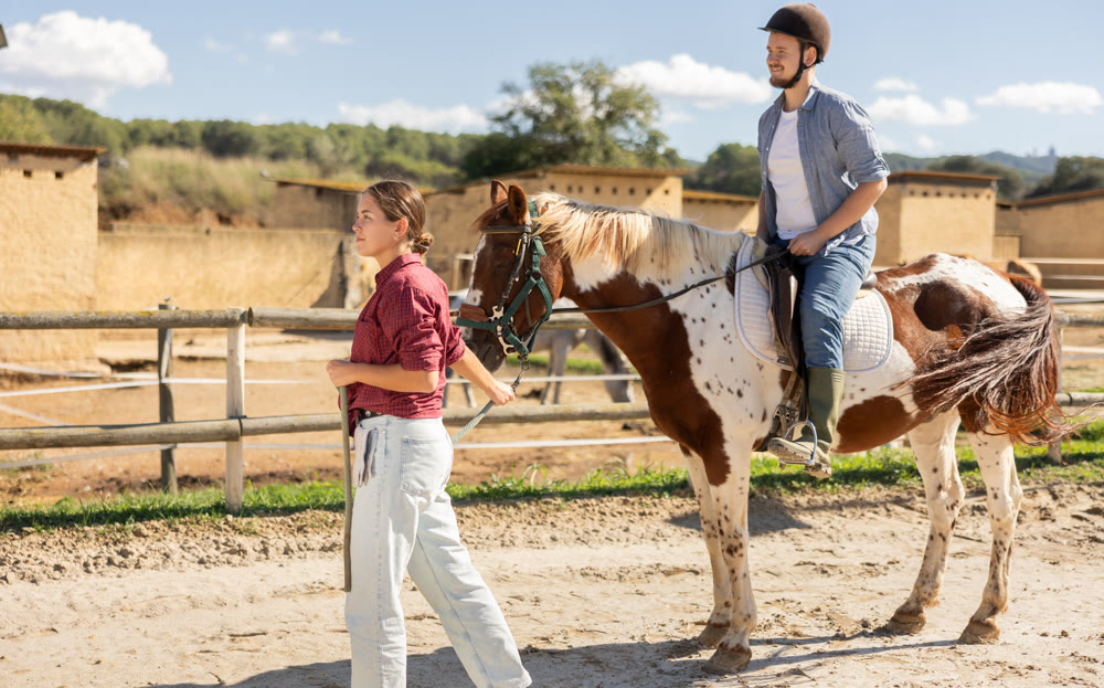 Young woman leading horse with man riding