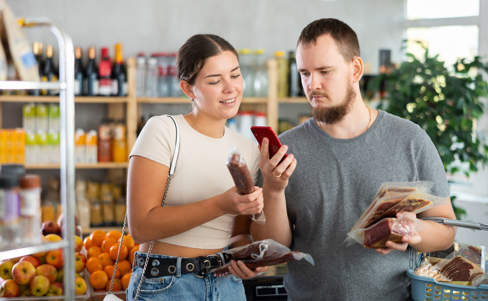 Portrait of man and woman checking the expiration date of dried sausage and jamon using smartphone