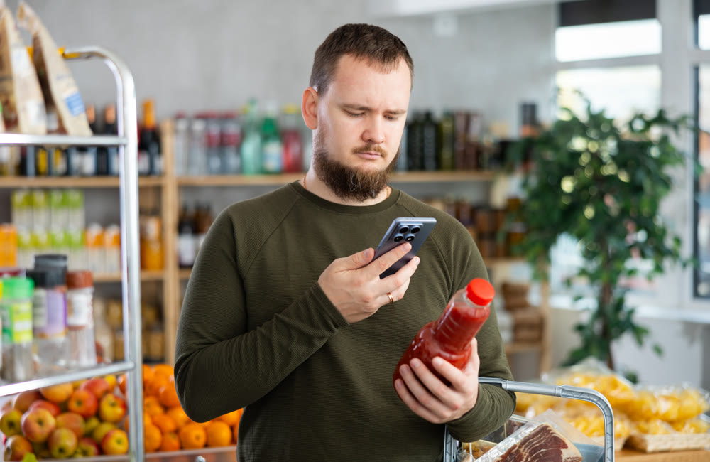 Male shopper scans QR code on the label of bottle tomato in supermarket