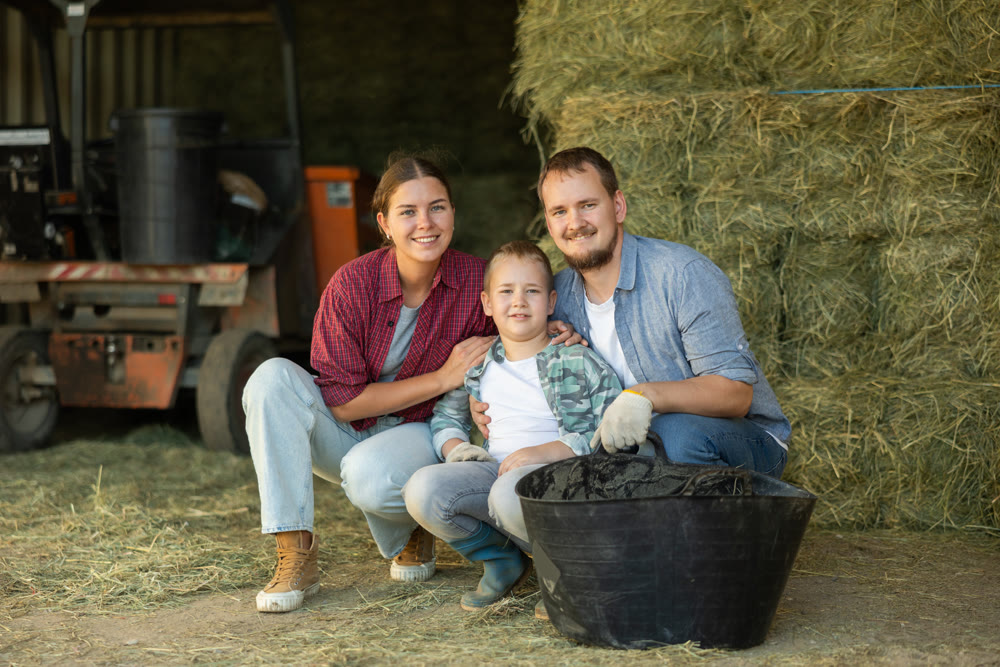 Man, woman and boy with bucket of hay in barn