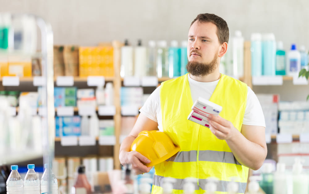 Young man builder chooses paracetamol at pharmacy