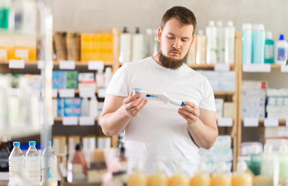 Young man chooses ointment at pharmacy
