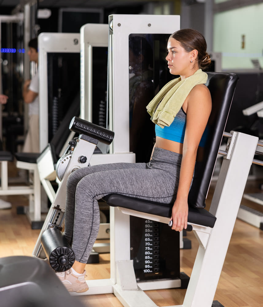 Young woman in gym performs exercises for leg muscles using simulators and fitness center equipment.