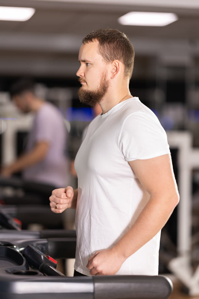 Focused bearded man works out with treadmill during class at fitness club