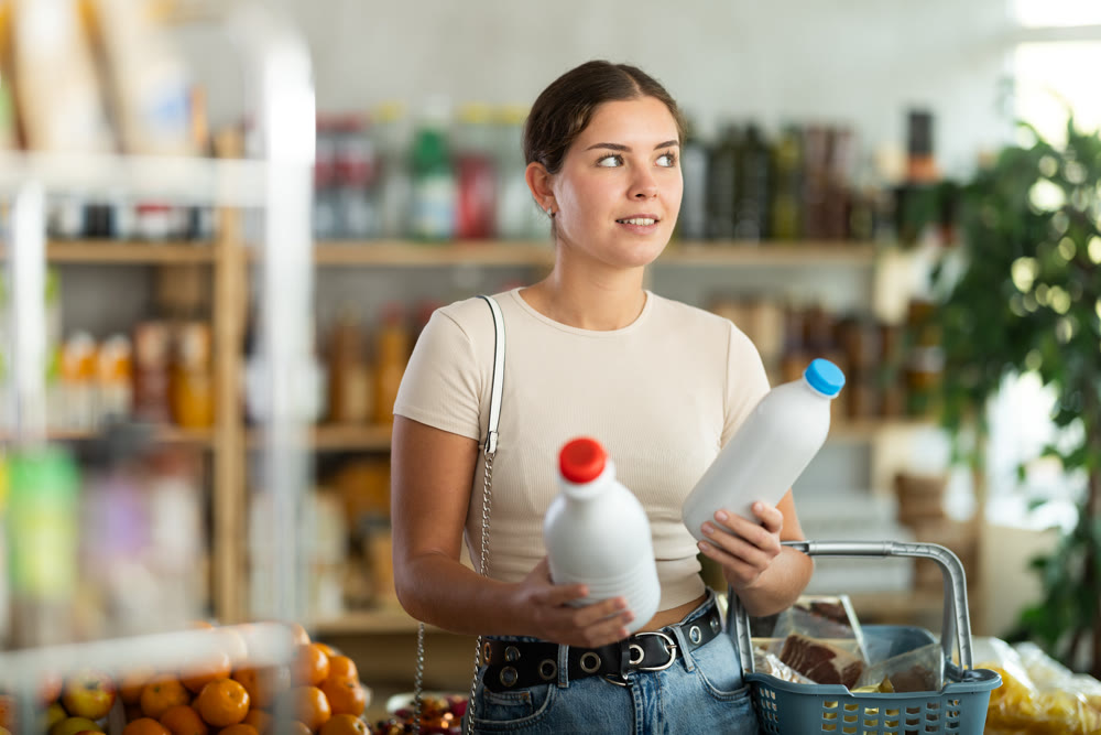Girl hold packages bottles and choose consider milk in store