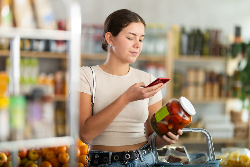 European woman customer at shop scans QR code on pickled tomatoes jar using phone camera