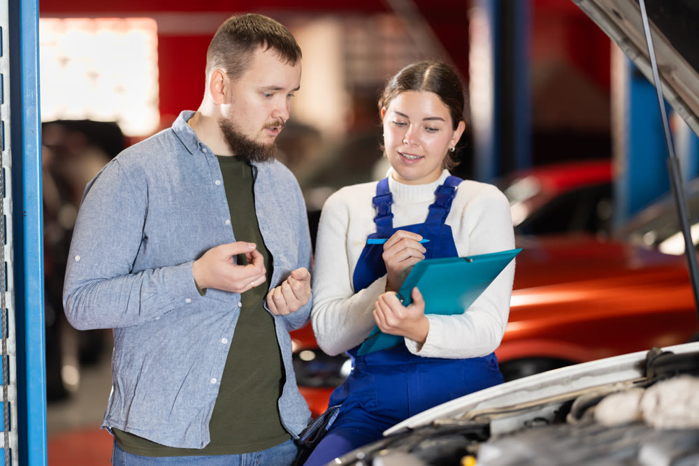 Female worker of auto service speaking to male client concerning notes wrote down on paper