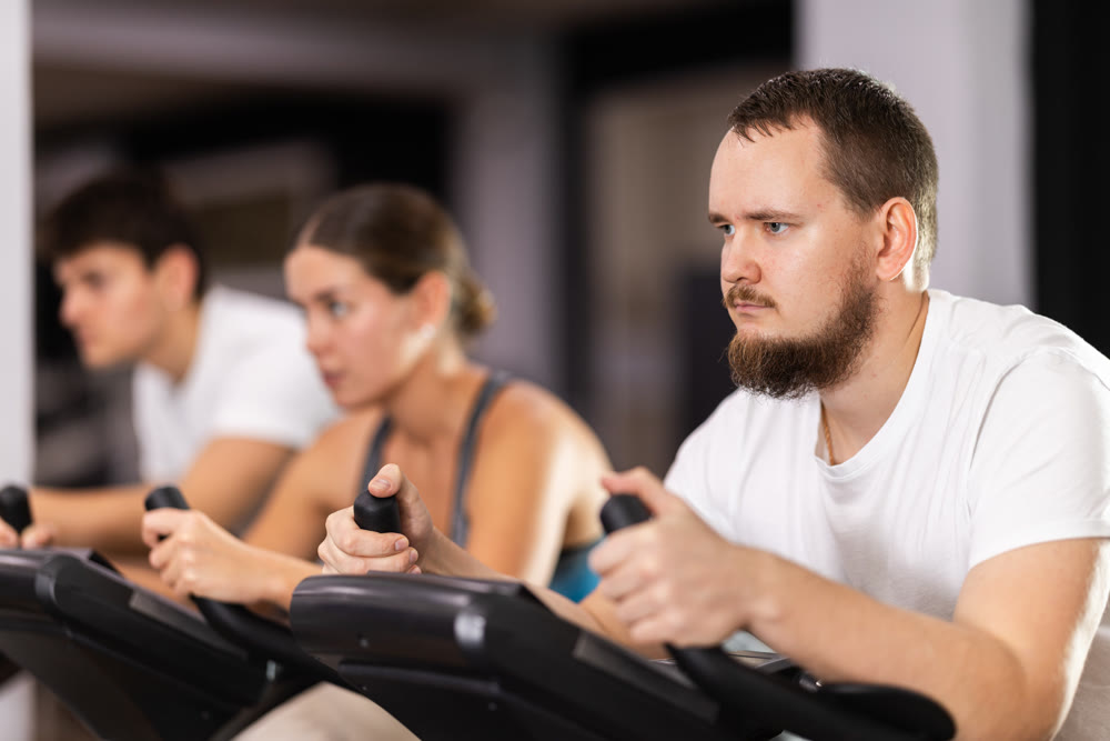 Focused bearded man works out with stationary bicycle during class at fitness club