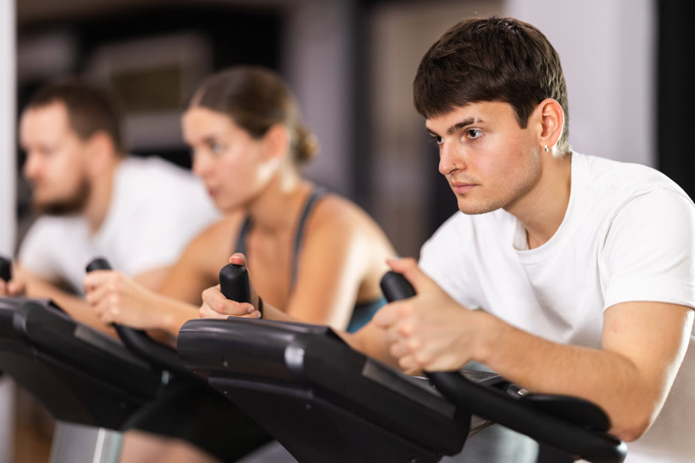 Focused guy works out with stationary bicycle during class at fitness club