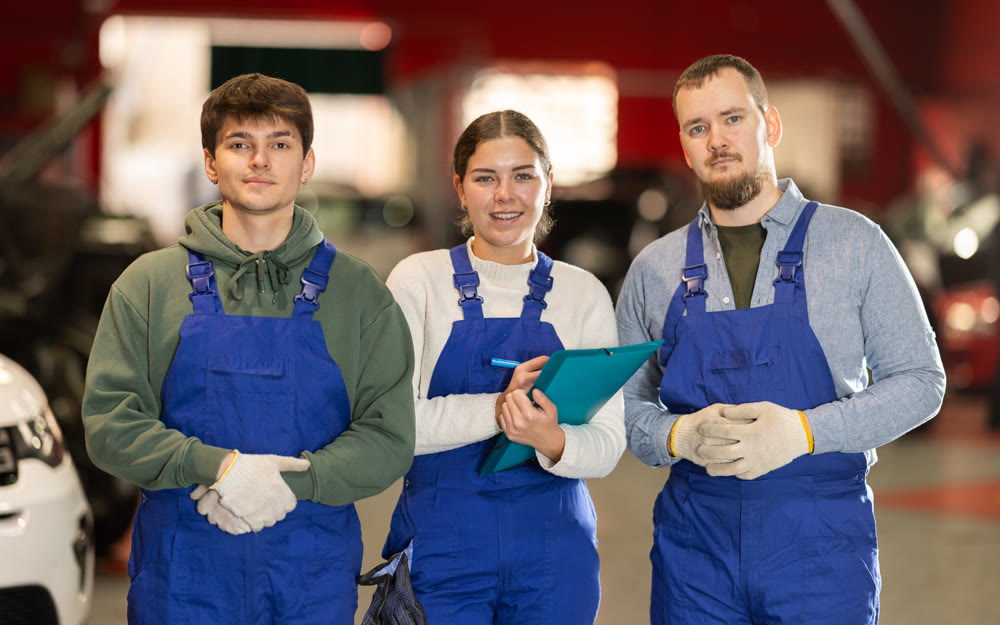 Team of auto mechanics, two men and one woman, wearing blue overalls and posing, ready to provide professional vehicle service