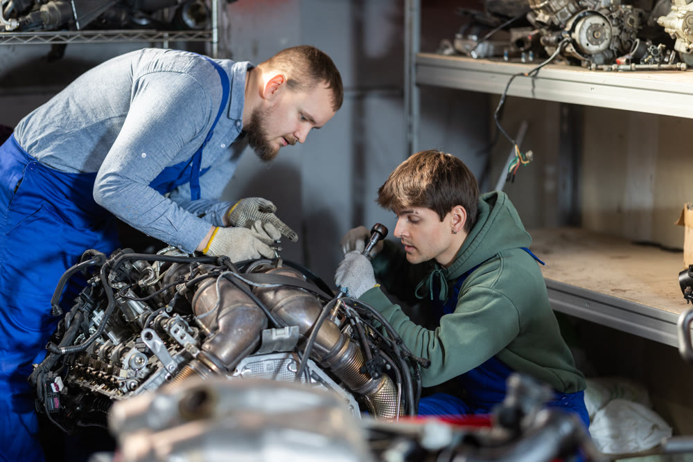 Two auto mechanics disassemble a car engine together for repair in garage